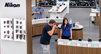 Camera Experience Shop. Best Buy store associate helping a customer try out a camera in a store.