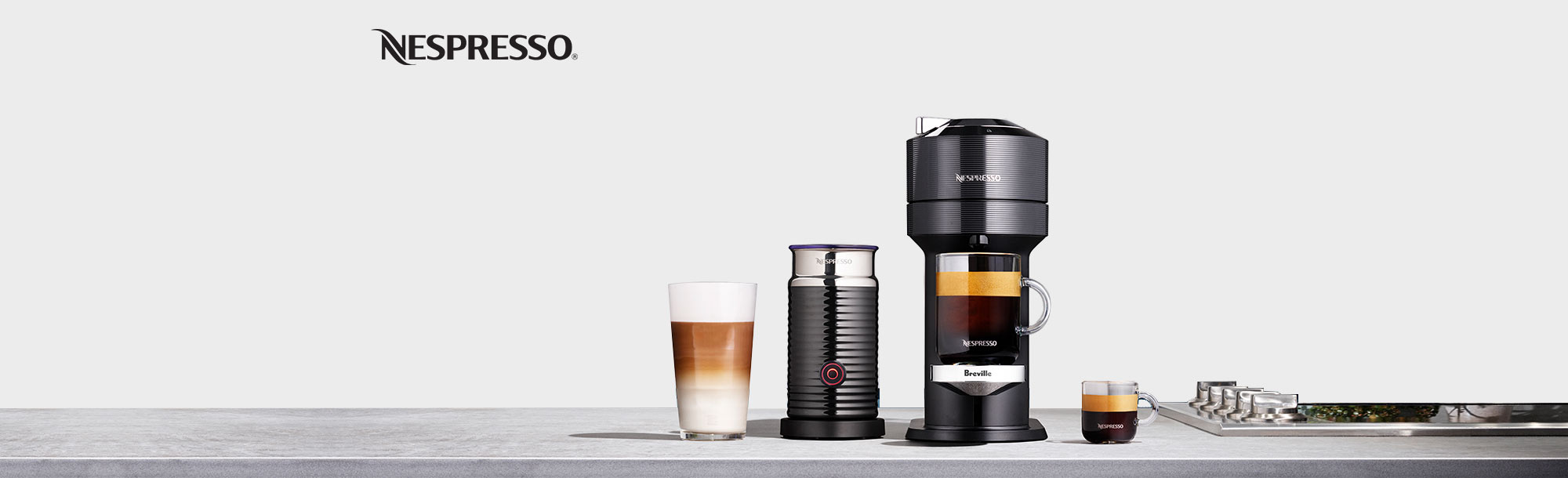 Kitchen counter with a coffee maker, milk frother, cup of espresso and coffee drink