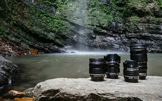 Camera lenses on rock with waterfall in background