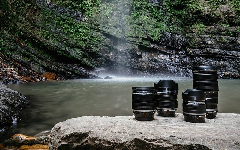Camera lenses on rock with waterfall in background