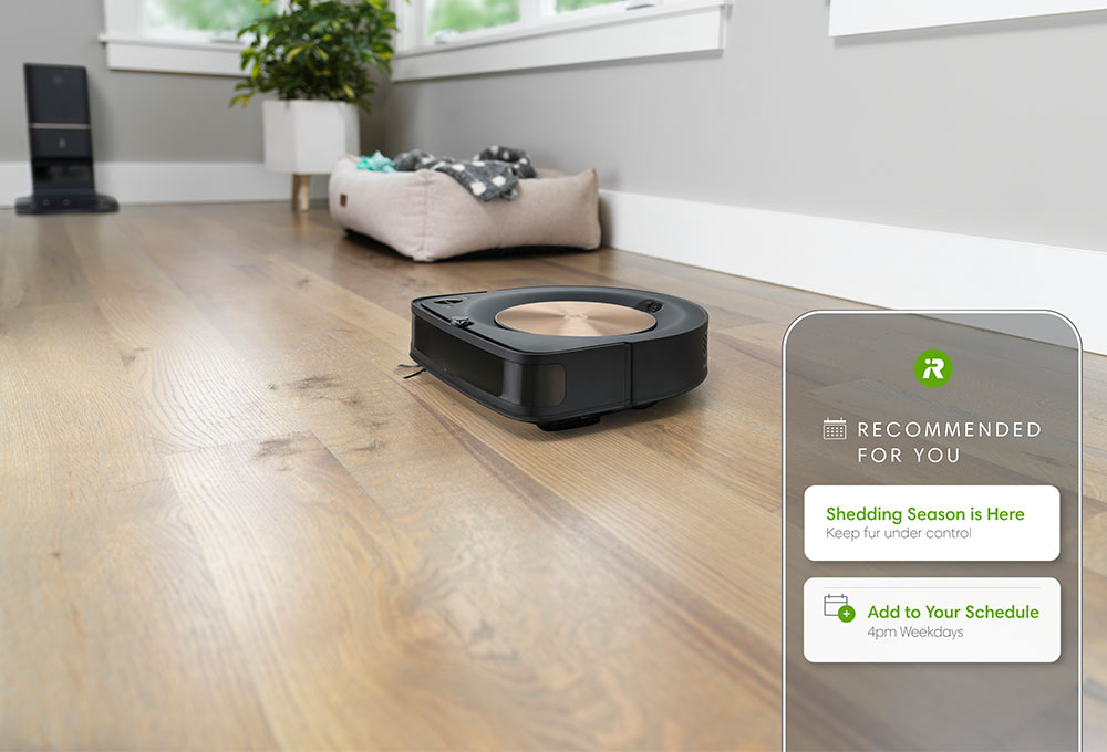 Robot vacuum on hardwood floor, smartphone with app that reads “Recommended for you. Shedding season is here; keep fur under control. Add to your schedule; 4 p.m. Wednesdays.