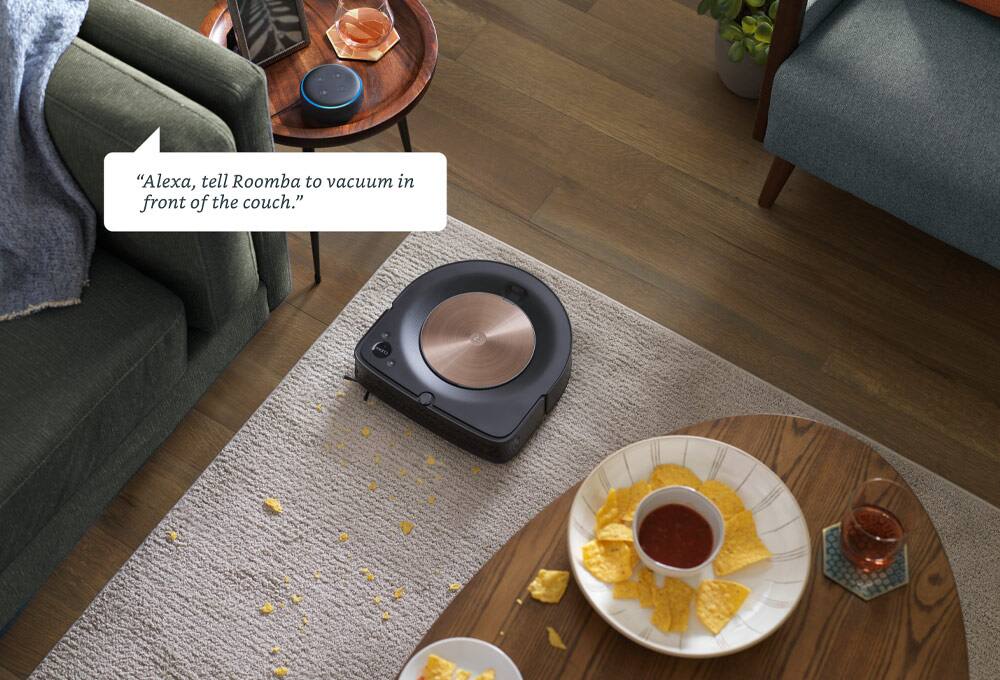 “Alexa, tell Roomba to vacuum in front of the couch.” Robot vacuum near chips spilled in front of couch.