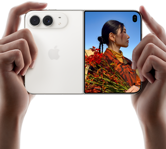 iPhone Duo, Star White color, held by two hands in horizontal orientation, unfolded, left panel shows 48MP Dual Fusion rear cameras, right panel shows person getting their picture taken on outer display, the subject of the photo is able to see their face as their picture is getting taken using Duo Preview