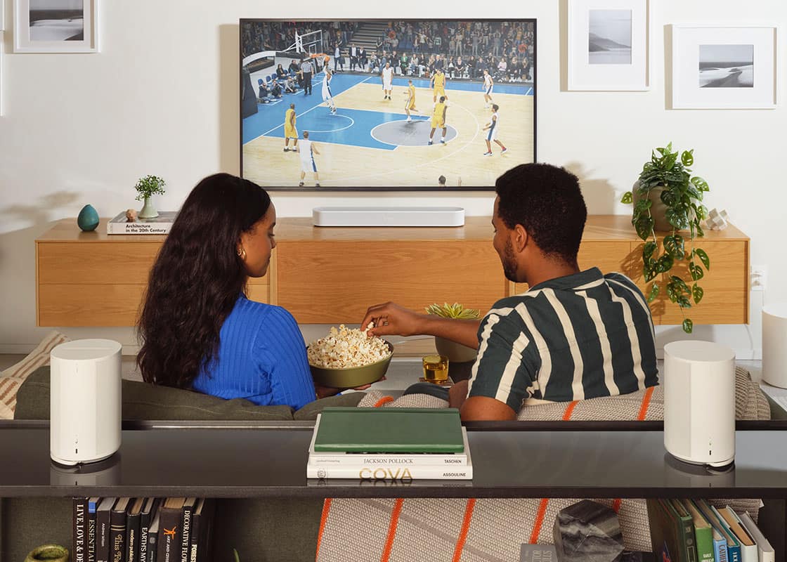 People watching TV with Sonos Era 100 Wi-Fi and Bluetooth Smart speakers.
