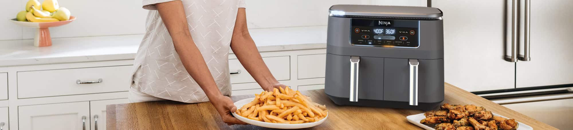 Person serving French fries and chicken wings near an air fryer
