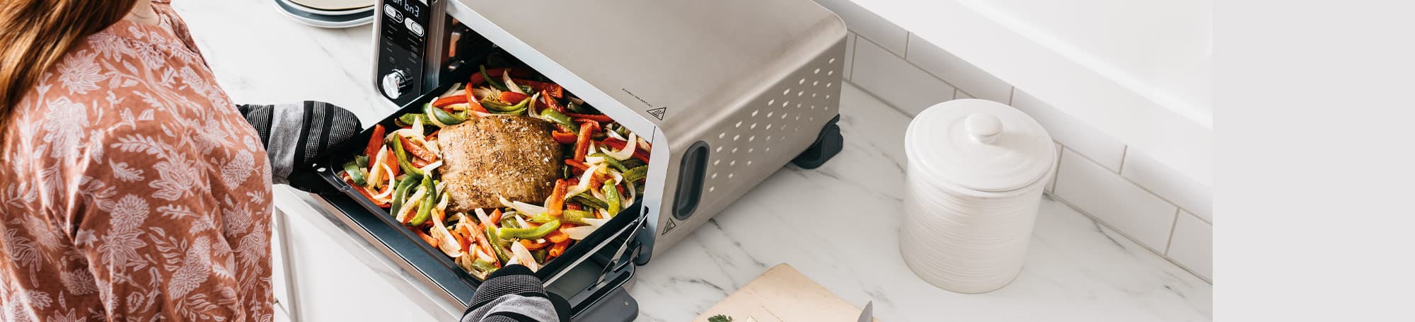 Person holding tray of food by toaster oven