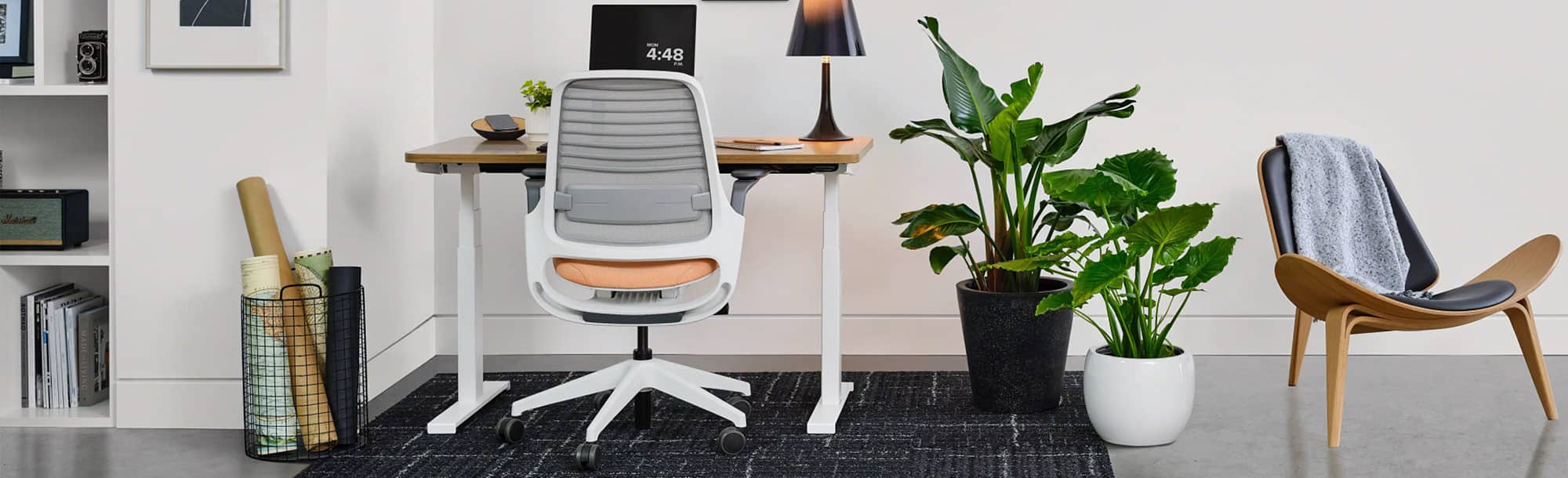 Back view of light-colored standing desk in lower position in home office with white, gray and peach chair