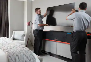 Geek Squad Agents installing a TV in a hotel room