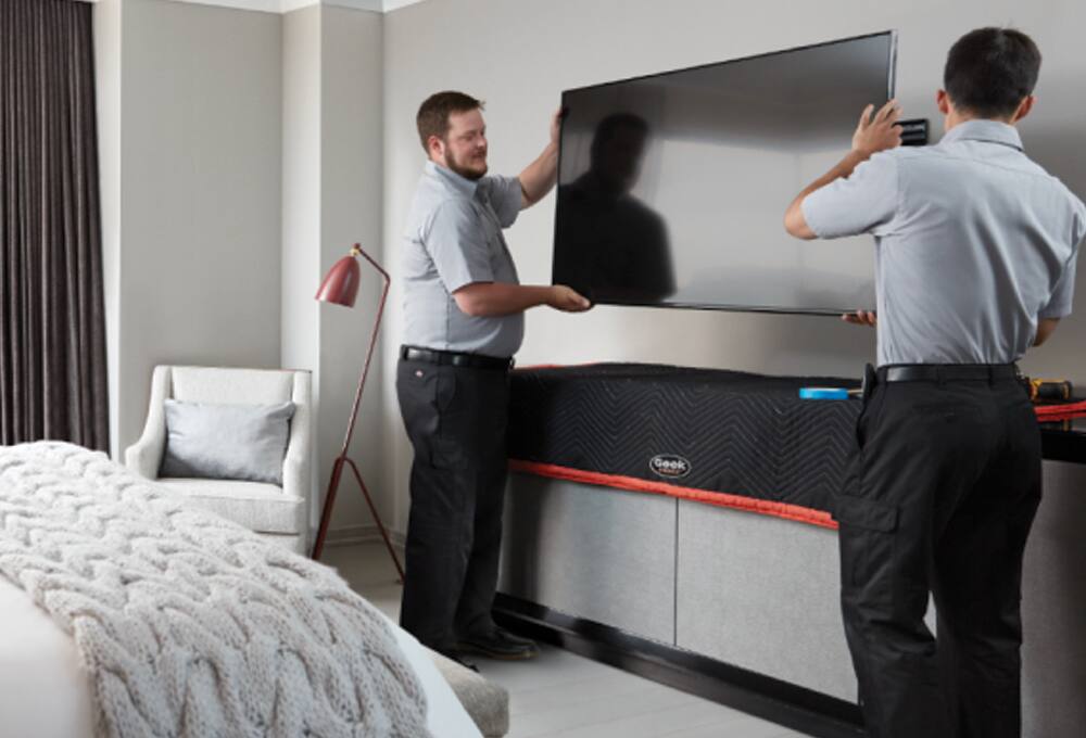 Geek Squad Agents installing a TV in a hotel room