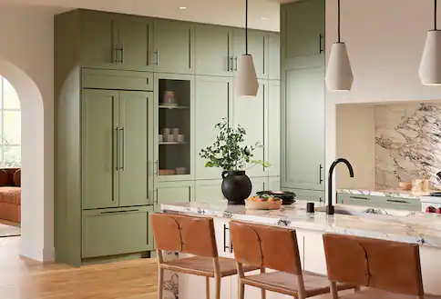 Green refrigerator flush with green cupboards, white countertops and island with brown chairs