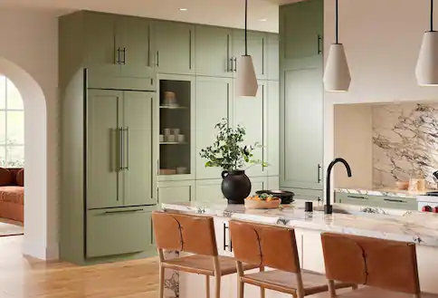 Green kitchen cupboards and refrigerator, white countertops and island with brown chairs