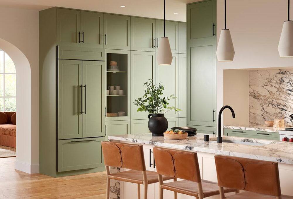 Green kitchen cupboards and refrigerator, white countertops and island with brown chairs