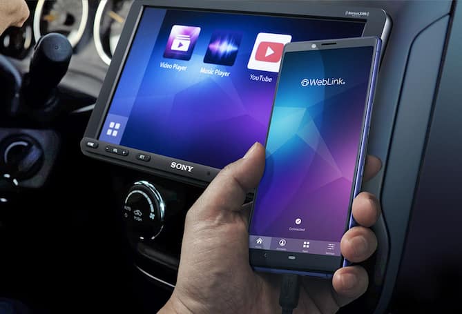 Person in a car’s passenger seat holding their phone. Their phone shows the same image as car receiver display