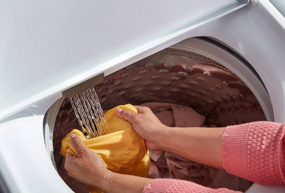 Interior of washer with faucet running water on clothing held by person