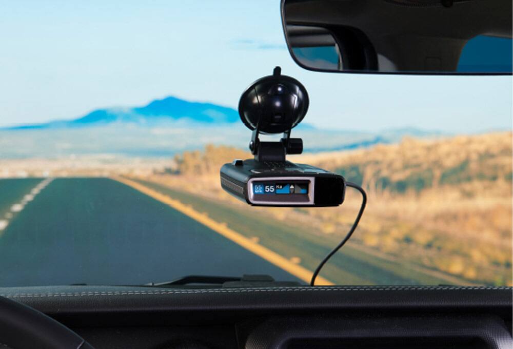 Radar detector attached to windshield with mountains and fields in background