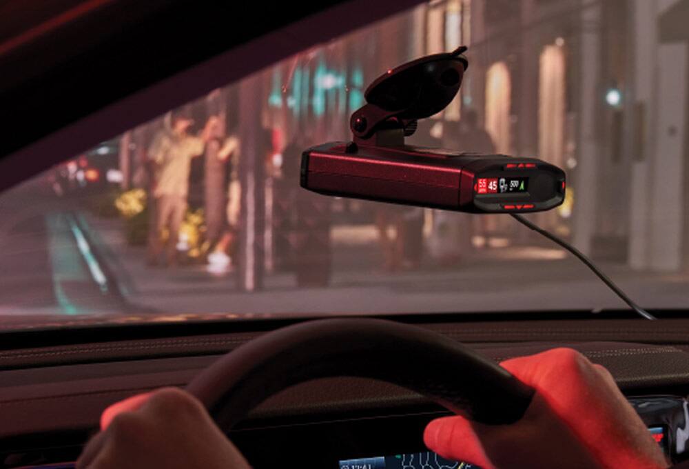 Radar detector attached to windshield with a busy city street in background