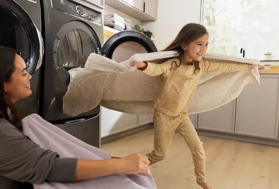 Child running from washer and dryer with blanket used as cape