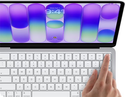 MacBook Neo, silver color, showing login screen, person's finger on Touch ID sensor in top-right corner of keyboard