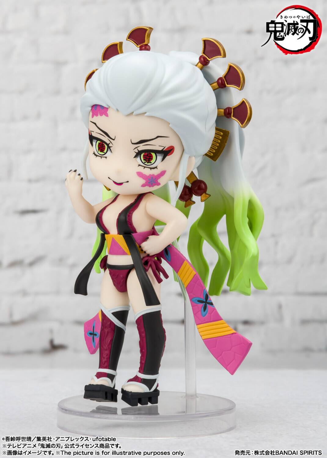 The image shows a figurine of a character with long white hair styled in a high ponytail, adorned with red and gold hair accessories. The character has a confident expression with a slight smile, featuring intricate facial markings and tattoos. She is wearing a deep V-neck top with a pink and yellow sash, paired with a matching skirt and thigh-high boots. The figurine is displayed on a clear stand against a plain background. The text on the image includes:

- "ufotable"
- "BANDAI SPIRITS"
- "The picture is for illustrative purposes only."
- Japanese text: "鬼滅の刃" (Kimetsu no Yaiba)
- "ufotable" and "BANDAI SPIRITS" at the bottom.