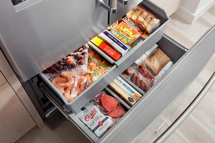 The image shows a refrigerator with its door open, revealing a variety of food items stored in the door compartments. The food items include a bag of sesame seeds, a bag of grains, a bag of mango bowl, a bag of spicy Thai, a bag of Hilary's bowl, a bag of shrimp, and a bag of chicken. The refrigerator is filled with an assortment of foods, providing a diverse selection for meal preparation.