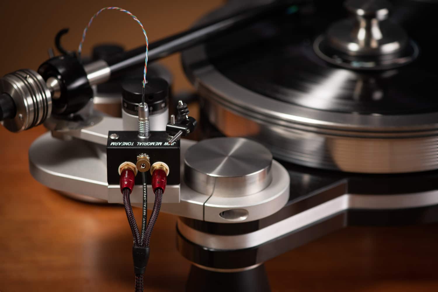 The image features a record player with a tonearm and a metal speaker. The tonearm is connected to a metal-speaker amplifier, which is designed to enhance the sound quality of the record player. The amplifier is placed on a wooden table, and the record player is ready to play.
