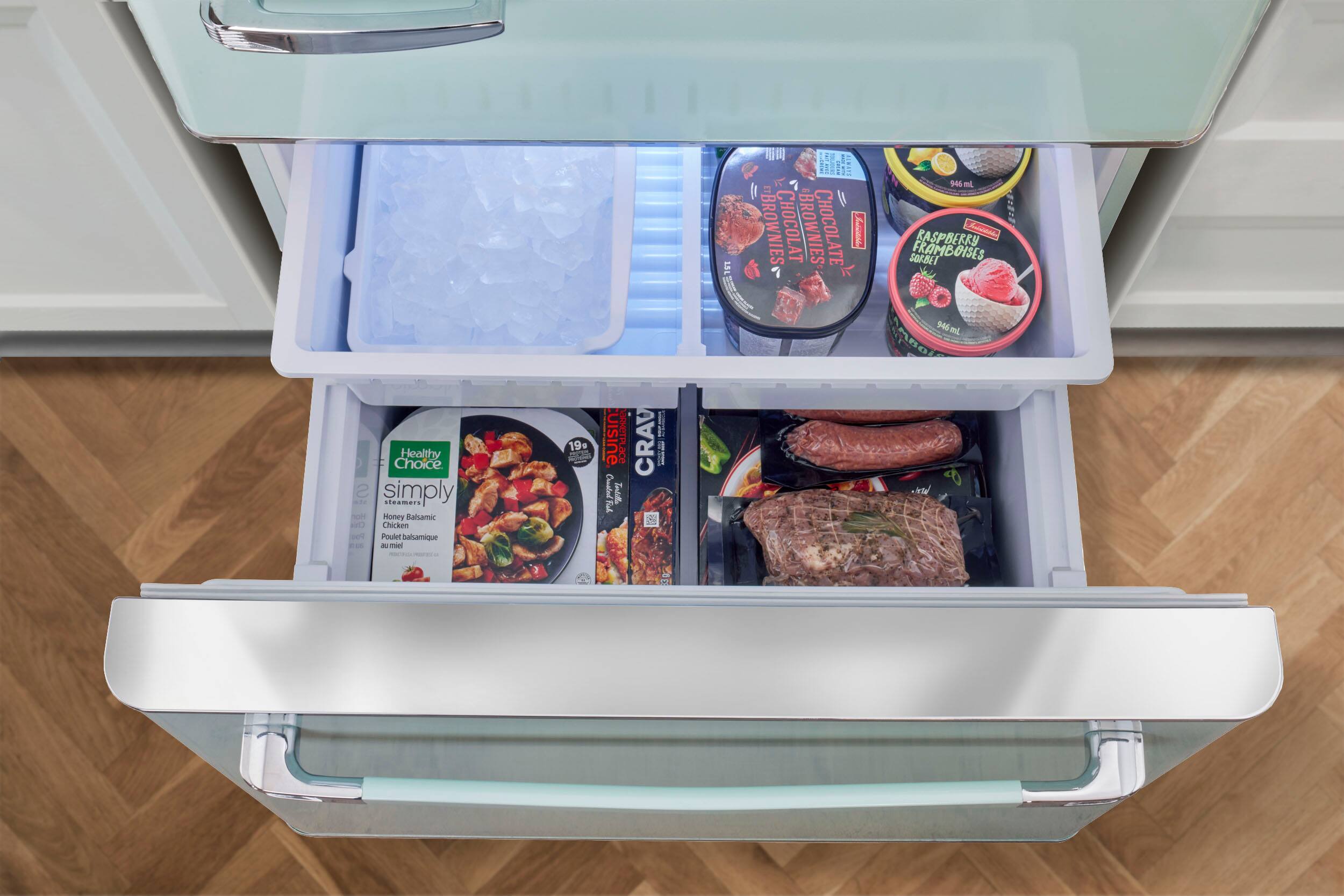 The image shows an open refrigerator with a variety of food items inside. There are several bowls containing different types of food, such as chicken, raspberries, and ice cream. The refrigerator also has a tray of ice cream and a tray of frozen vegetables. The refrigerator is filled with a diverse assortment of food items, making it a well-stocked and convenient place for meal preparation.