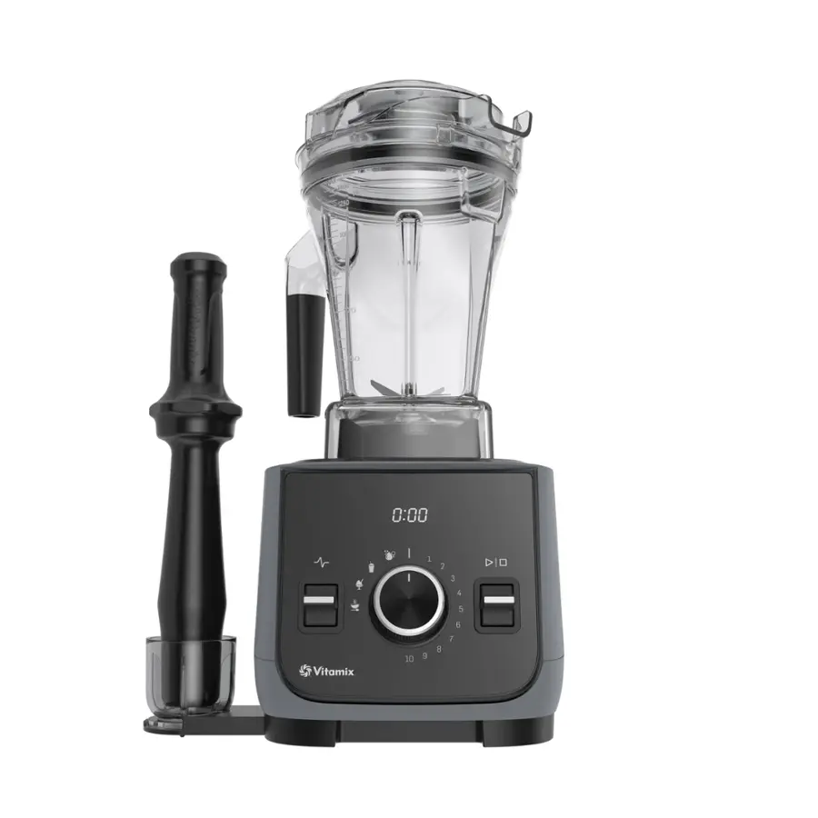 The image features a Vitamix blender with a black handle and a black base. The blender is sitting on a countertop, and the lid is off. The blender is accompanied by a black handle, which is placed next to it. The blender is turned on, and the timer reads 0:00.