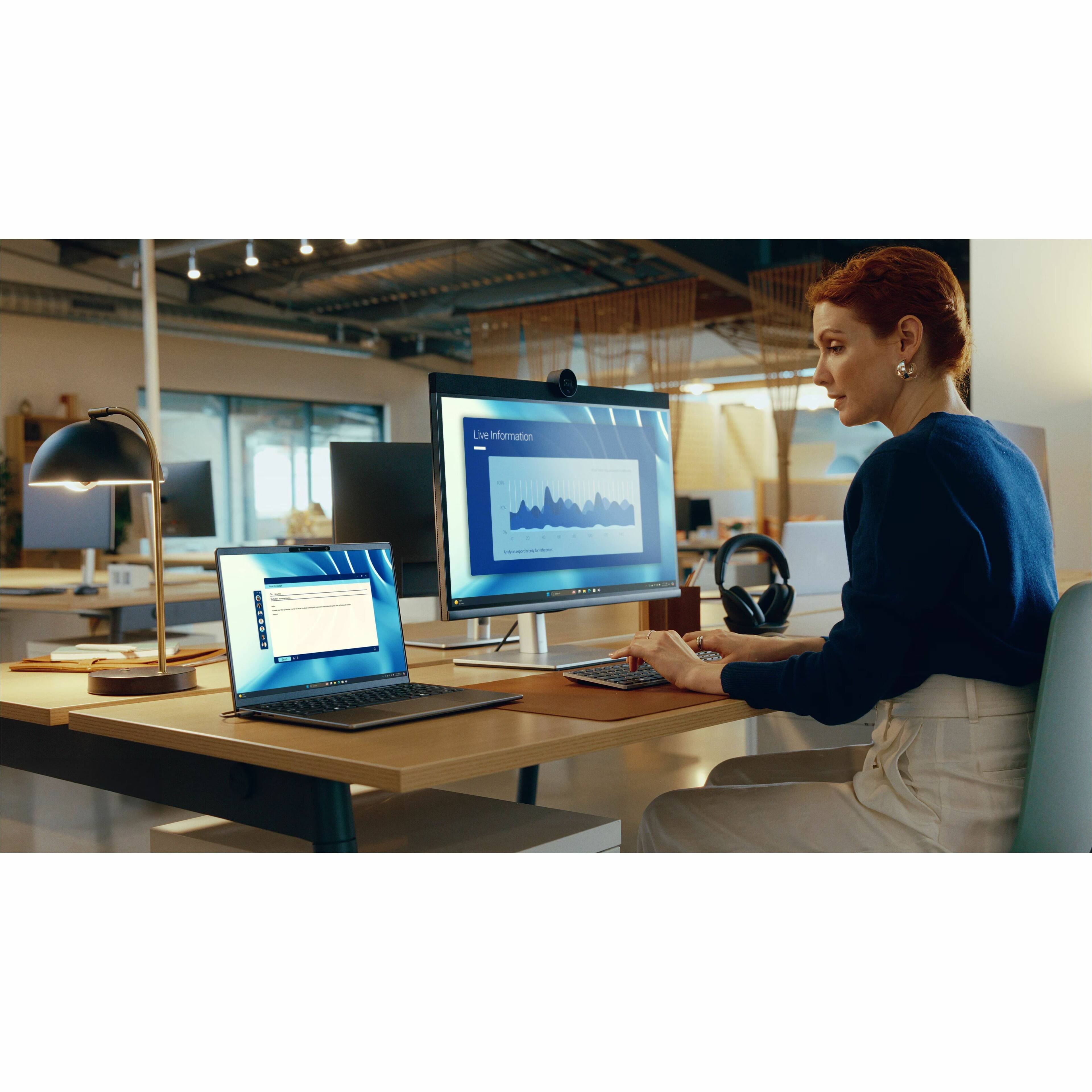 The woman is sitting at a desk with a laptop and a large monitor in front of her. She is using the laptop and the monitor simultaneously, possibly for multitasking or enhancing her work experience. The desk also has a keyboard and a mouse, which she is using to interact with the computer. The scene suggests that she is working in a professional setting, such as an office or a home office.