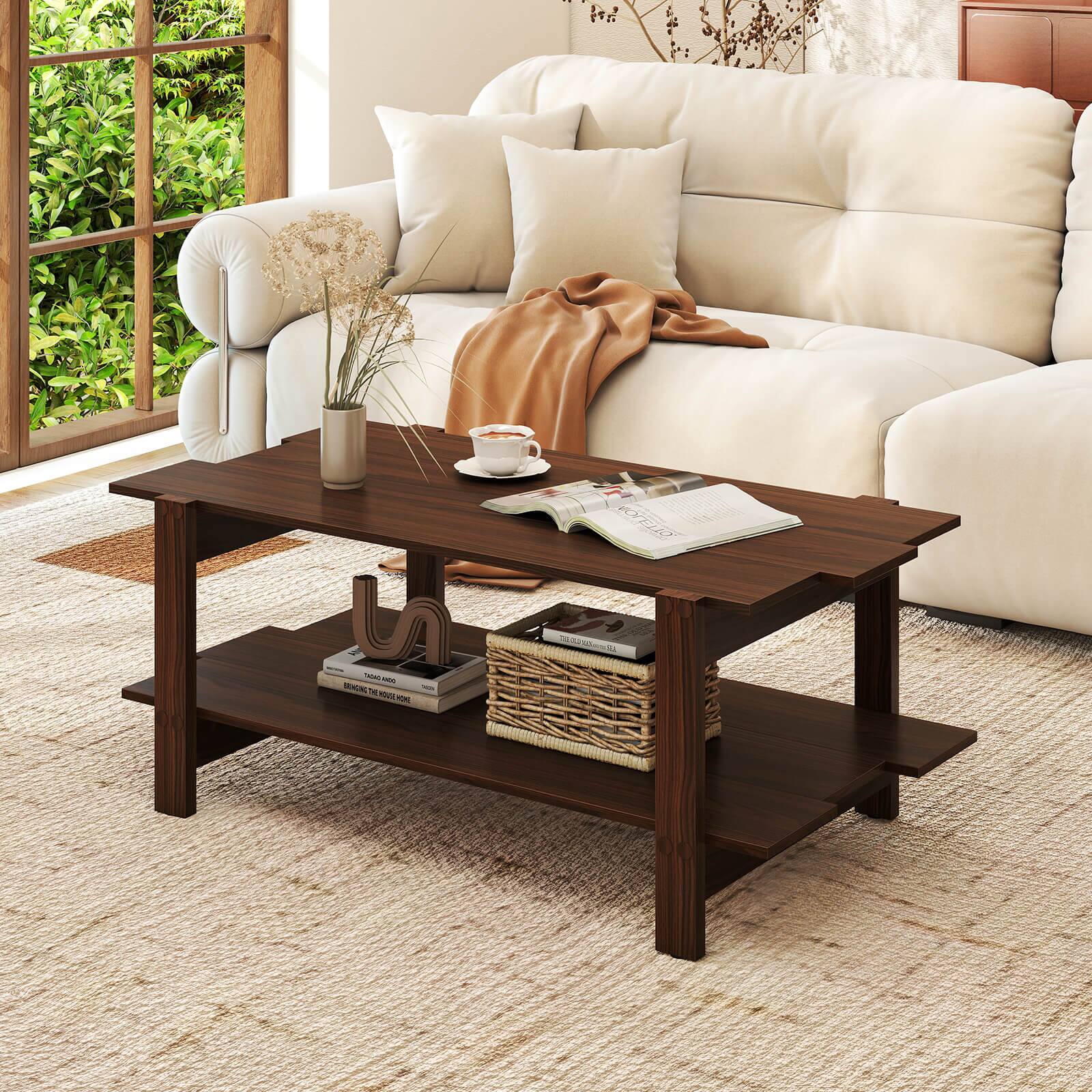 The image shows a living room with a white couch, a coffee table, and a window. The coffee table has a vase, a cup, and a book on it. The vase is located on the left side of the table, and the cup is placed closer to the center. The book is positioned towards the right side of the table. The couch is situated in the background, occupying a significant portion of the room. The living room appears to be well-organized and inviting, with a focus on comfort and relaxation.