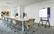 The image shows a conference room with a large screen TV mounted on the wall. The TV is displaying data and graphs, which suggests that it is being used for a presentation or meeting. The room is furnished with multiple chairs, some of which are arranged around the TV, and a dining table. There are also several potted plants placed throughout the room, adding a touch of greenery to the space. The overall atmosphere of the room appears to be professional and conducive to collaboration and discussion.