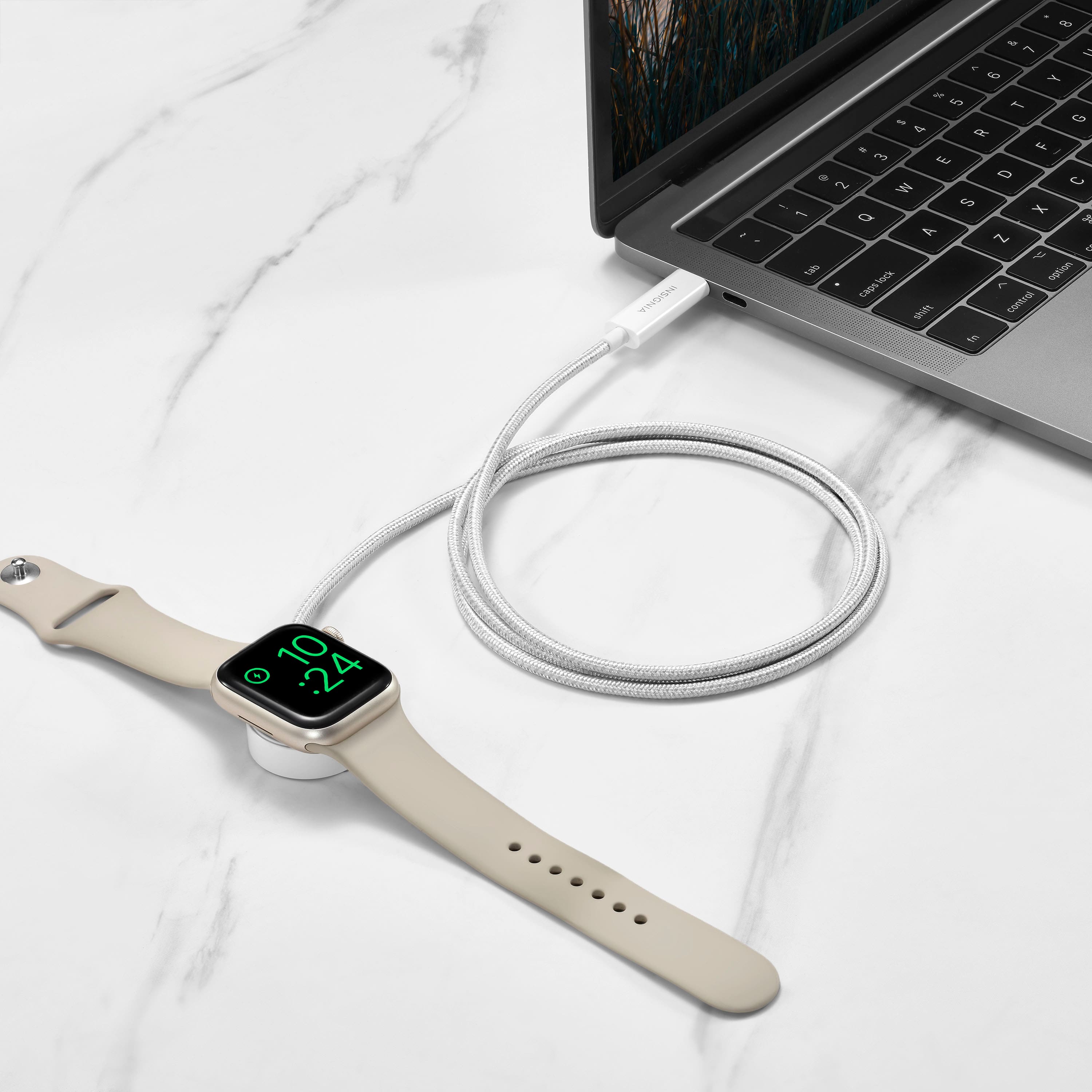 The image shows a watch with a face that reads 10:24. The watch is connected to a laptop, which is sitting on a desk. The laptop is open, and the watch is connected to it via a wire. The scene suggests that the person wearing the watch is likely using the laptop for work or other tasks.