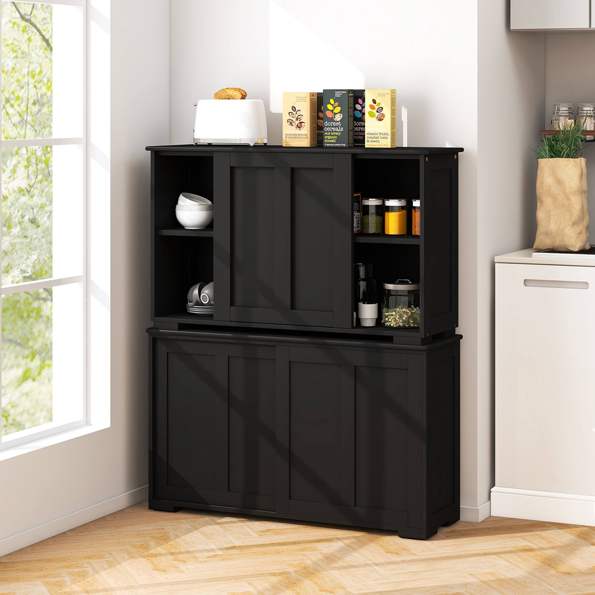 I see a black cabinet with a white toaster on top of it. There are also some coffee beans and a bag of coffee in the cabinet. Additionally, there are several spices and a potted plant nearby.