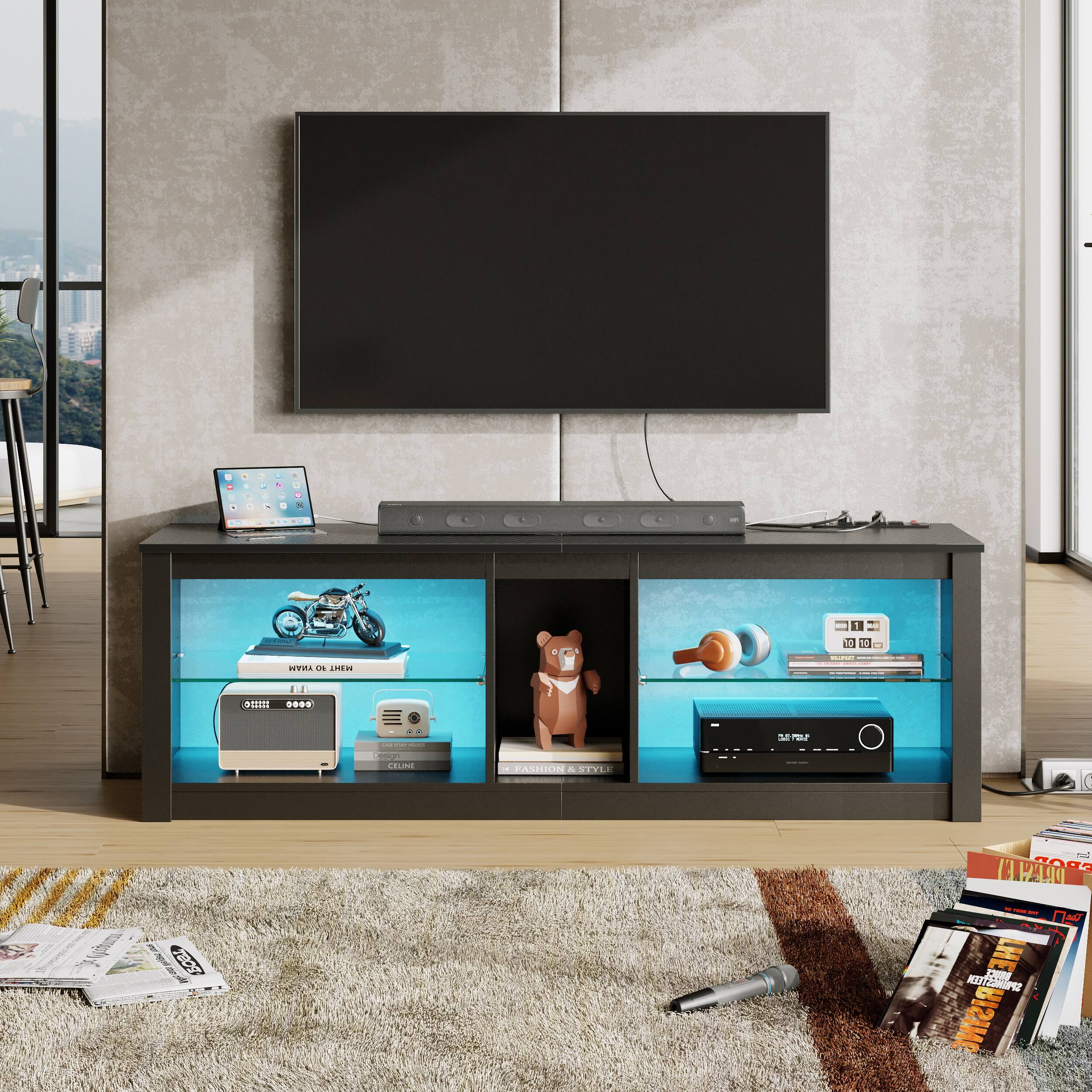 The image shows a living room with a flat screen TV mounted on the wall. The TV is surrounded by various items, including a laptop, a teddy bear, and several books. There is also a remote control placed nearby. The room features a comfortable couch and a dining table. The scene is set against a backdrop of a city view, giving the space a cozy and inviting atmosphere.
