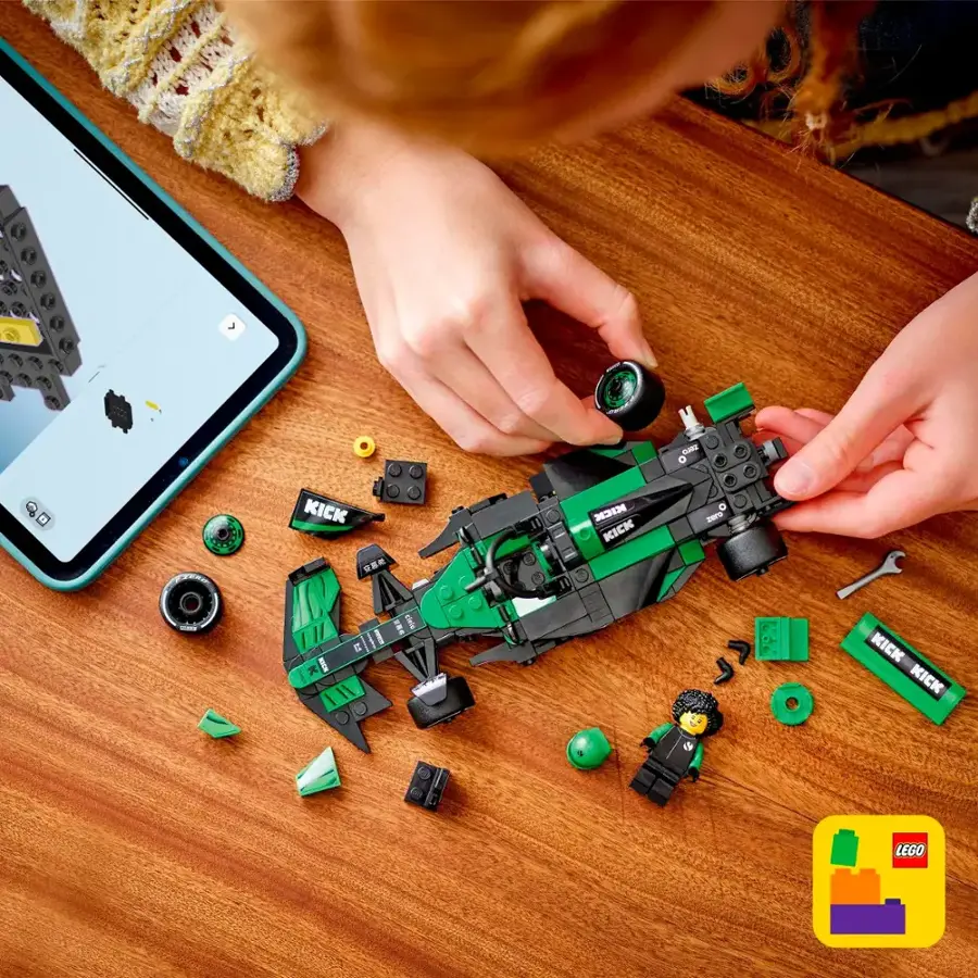 A person is sitting at a table, working on a green Lego car. They are using a tablet to follow instructions and assemble the car. The tablet is placed next to the Lego car, and the person is focused on the task at hand.