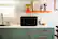 The text "12:20 Whipbal" is not present in the image. The image features a kitchen with a microwave, a sink, a counter, and a shelf with potted plants and a vase.