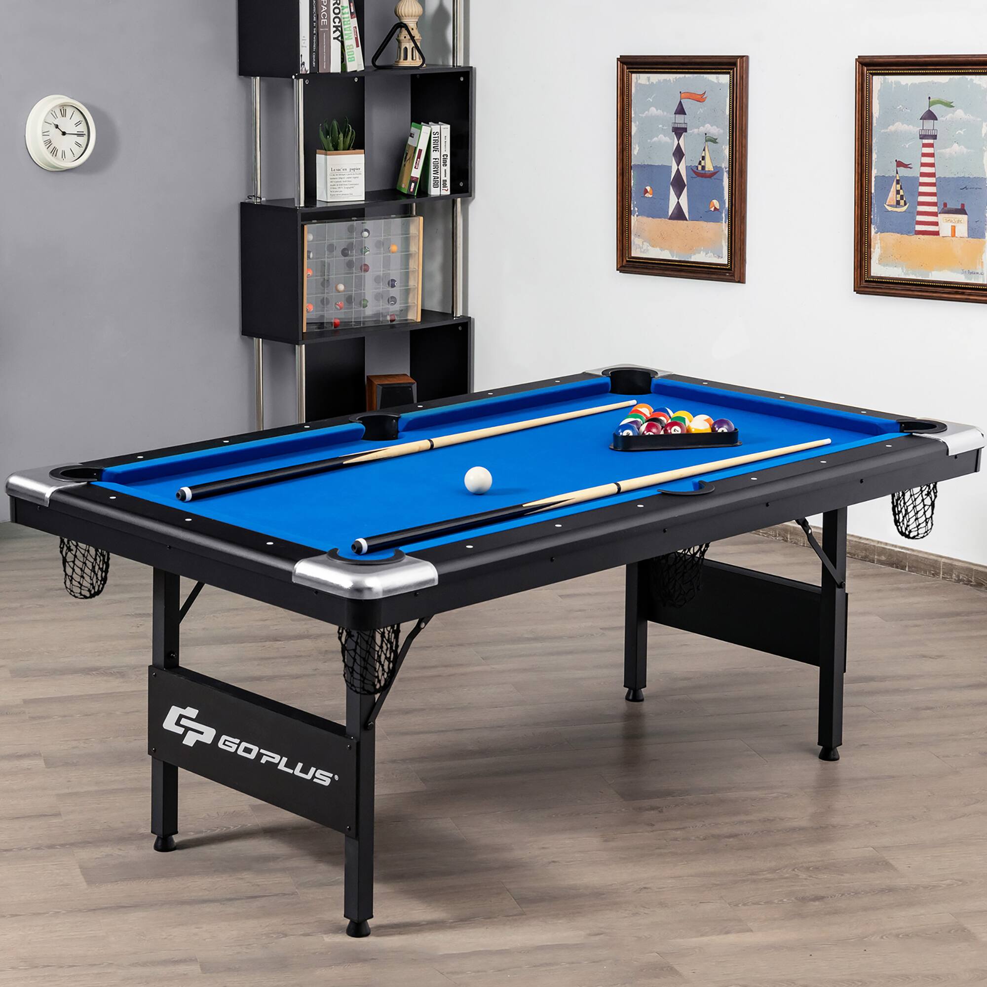 The image features a blue pool table with a black frame, placed in a room with hardwood floors. The table is surrounded by several books, and there are two pictures hanging on the wall. The table is well-equipped with a cue stick and a sports ball. The room also has a clock on the wall, adding to the overall ambiance of the space.