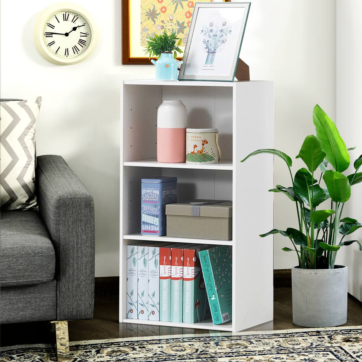 The image shows a small white bookshelf in a living room. The bookshelf is filled with various books, and there is a clock on the wall above it. Additionally, there is a potted plant in the room, adding a touch of greenery to the space. The books on the shelf are arranged in a way that makes efficient use of the limited space, showcasing a variety of sizes and colors. The combination of the bookshelf, clock, and potted plant creates a cozy and inviting atmosphere in the living room.