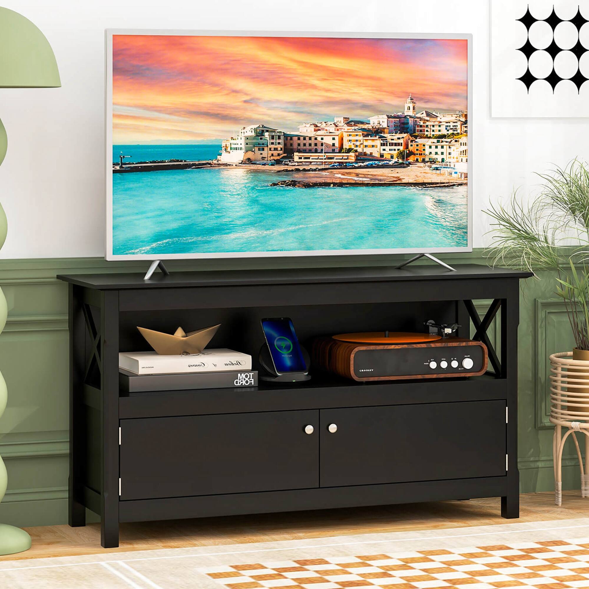The image shows a television sitting on top of a black entertainment center. The TV is displaying a picture of a cityscape, possibly a beach scene. The entertainment center has a shelf underneath the TV, where a laptop and a remote control are placed. There is also a potted plant nearby, adding a touch of greenery to the room.