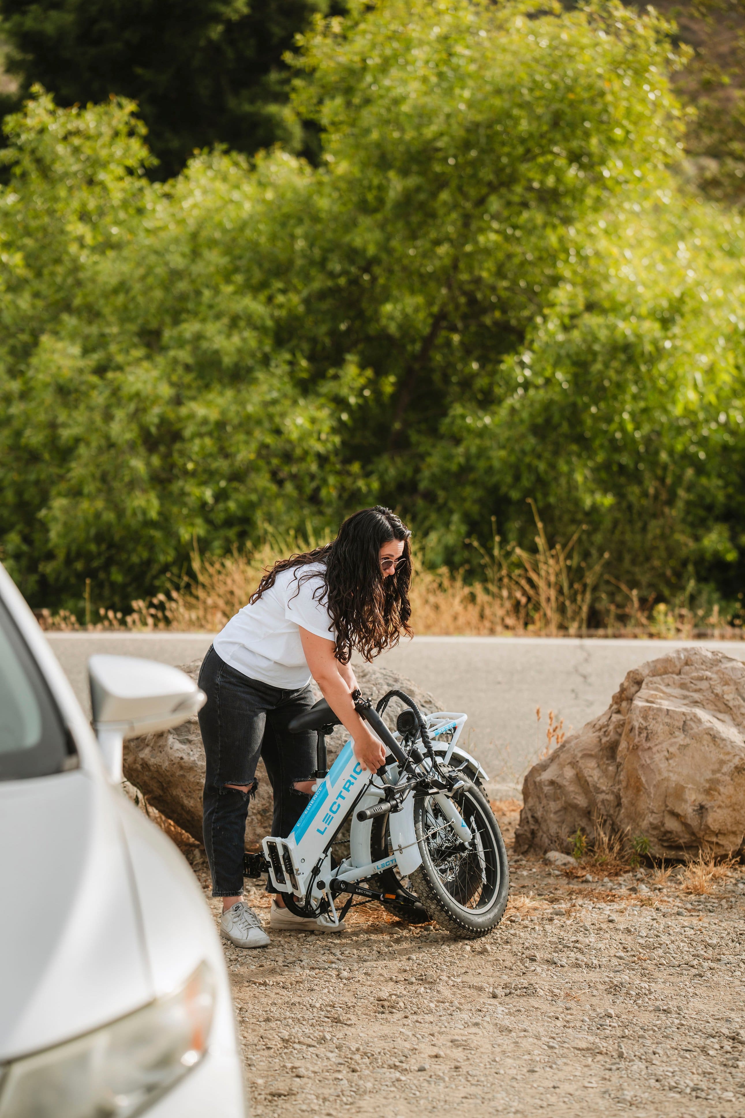 The text on the image reads "RENC Lectric Lect -". It seems to be an advertisement or a promotional message for an electric bicycle. The woman in the image is standing next to the bicycle, possibly checking it or preparing to ride it.