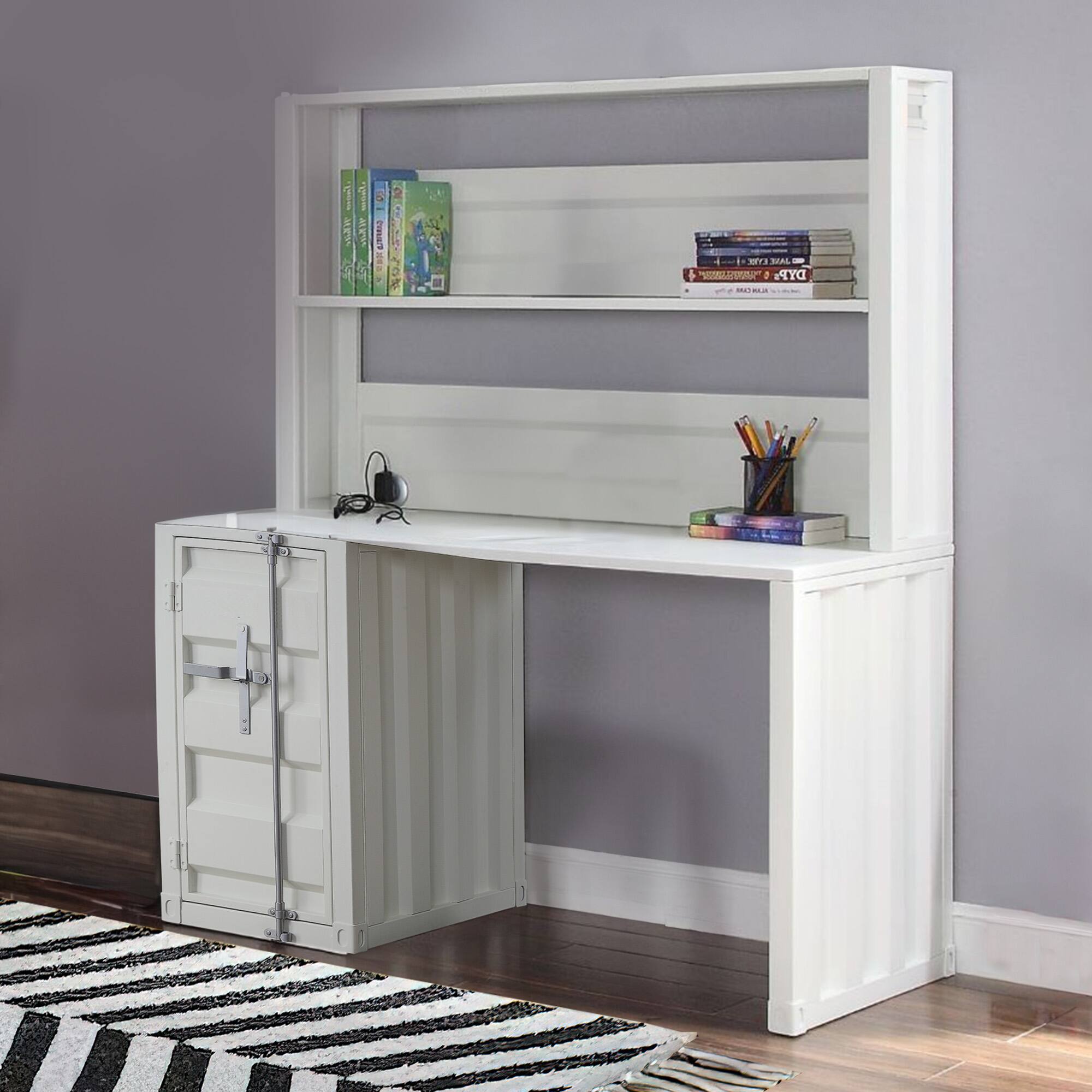 I see a white desk with shelves. On the top shelf, there are books, including one with a green cover. On the middle shelf, there are more books stacked. On the desk, there is a small speaker and a cup with pencils. The desk has a cabinet with two doors on the left side.