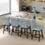 The image shows a kitchen with a marble countertop and a breakfast bar. There are four blue chairs placed around the bar, and a dining table is located nearby. The kitchen is well-equipped with a sink, oven, and microwave. Various items can be seen on the countertop, such as a bottle, wine glass, and bowl. Additionally, there are two apples and an orange placed on the countertop, adding a touch of color to the scene.