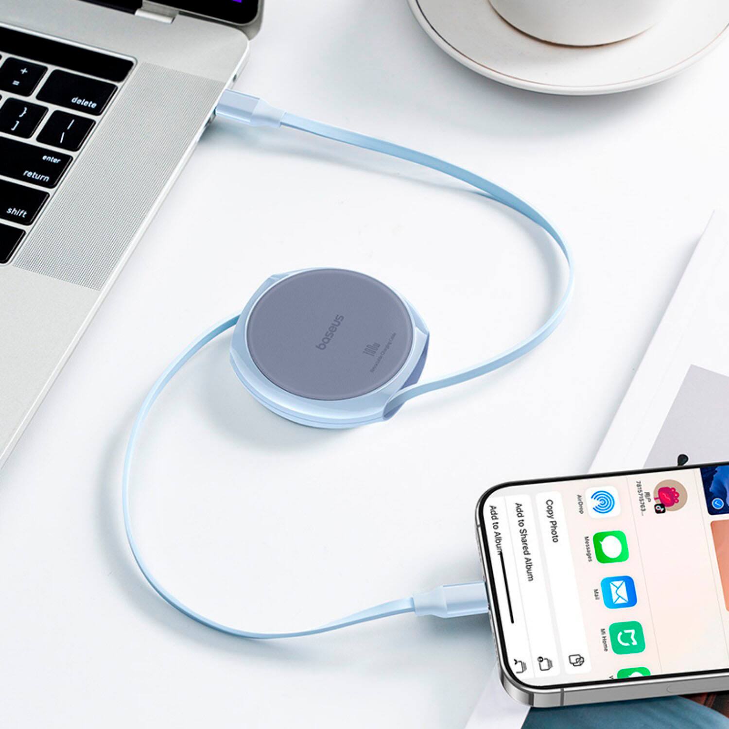 The image shows a cell phone connected to a laptop via a blue cord. The cell phone is placed on top of the laptop, and the laptop is sitting on a desk. There is also a cup nearby, possibly containing coffee.