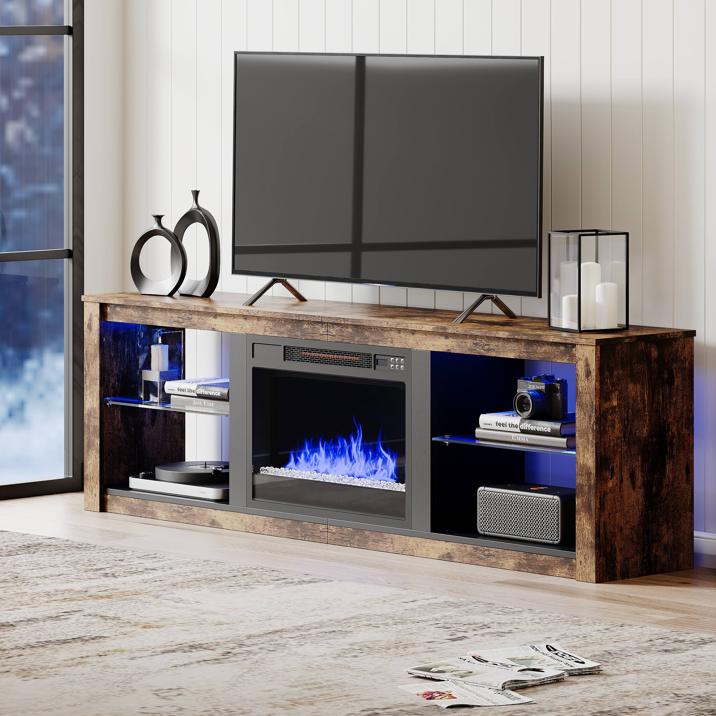A flat screen TV is sitting on top of a wooden entertainment center. The entertainment center features a fireplace and a speaker system. The TV is placed on a stand, and there are several books and a remote control nearby. The scene also includes a window, a candle, and a clock.