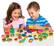 The image features two children sitting at a table, playing with a toy train set. They are surrounded by various toy pieces, including a train, a car, and a cup. The children are smiling and enjoying their time together, creating a fun and engaging atmosphere.