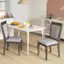 The image shows a dining table with two chairs placed around it. The table is set with a plate of food, including oranges, a bowl of fruit, and a cup. There are also two books on the table, possibly for reading during the meal. The scene is set in a kitchen area, with a sink visible in the background.