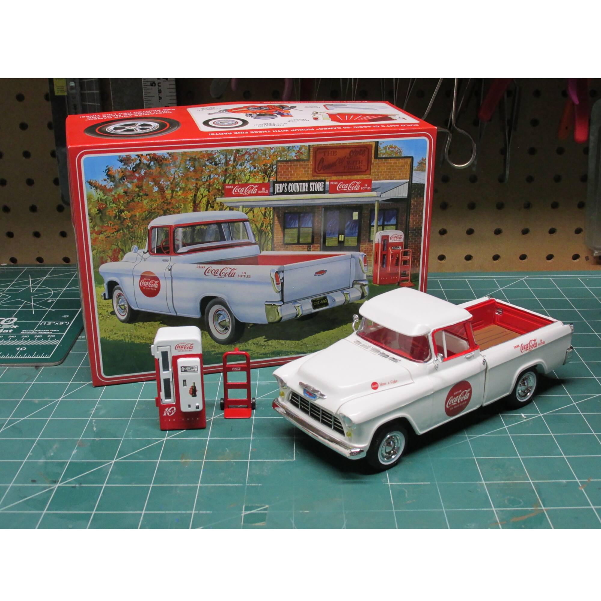 The image features a Coca-Cola truck and a gas pump. The truck is parked next to the gas pump, which is red and white. The scene is set on a table, and the truck is positioned in front of a Coca-Cola store. The truck is a toy, and it is accompanied by a small gas pump and a Coca-Cola sign. The combination of these elements creates a nostalgic and playful atmosphere, reminiscent of simpler times when gas stations and Coca-Cola were iconic symbols of Americana.