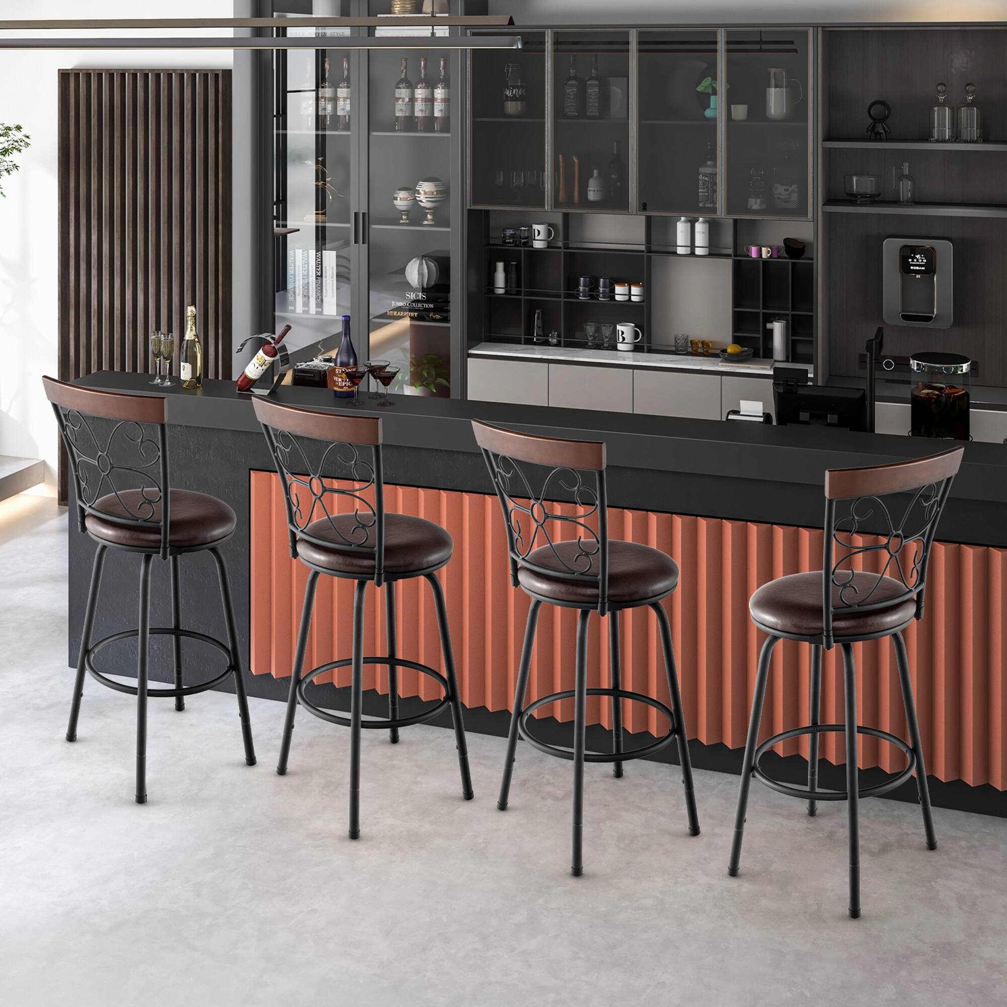 The image shows a modern kitchen or bar area with a sleek design. There are four bar stools with dark brown leather seats and black metal frames with decorative backrests. The counter is dark, and the back panel is a contrasting orange color. On the counter, there are two champagne glasses, a bottle of champagne, a wine bottle, and a cocktail glass. The shelves behind the counter are filled with various bottles, cups, and kitchen items. The overall setting is clean and contemporary.