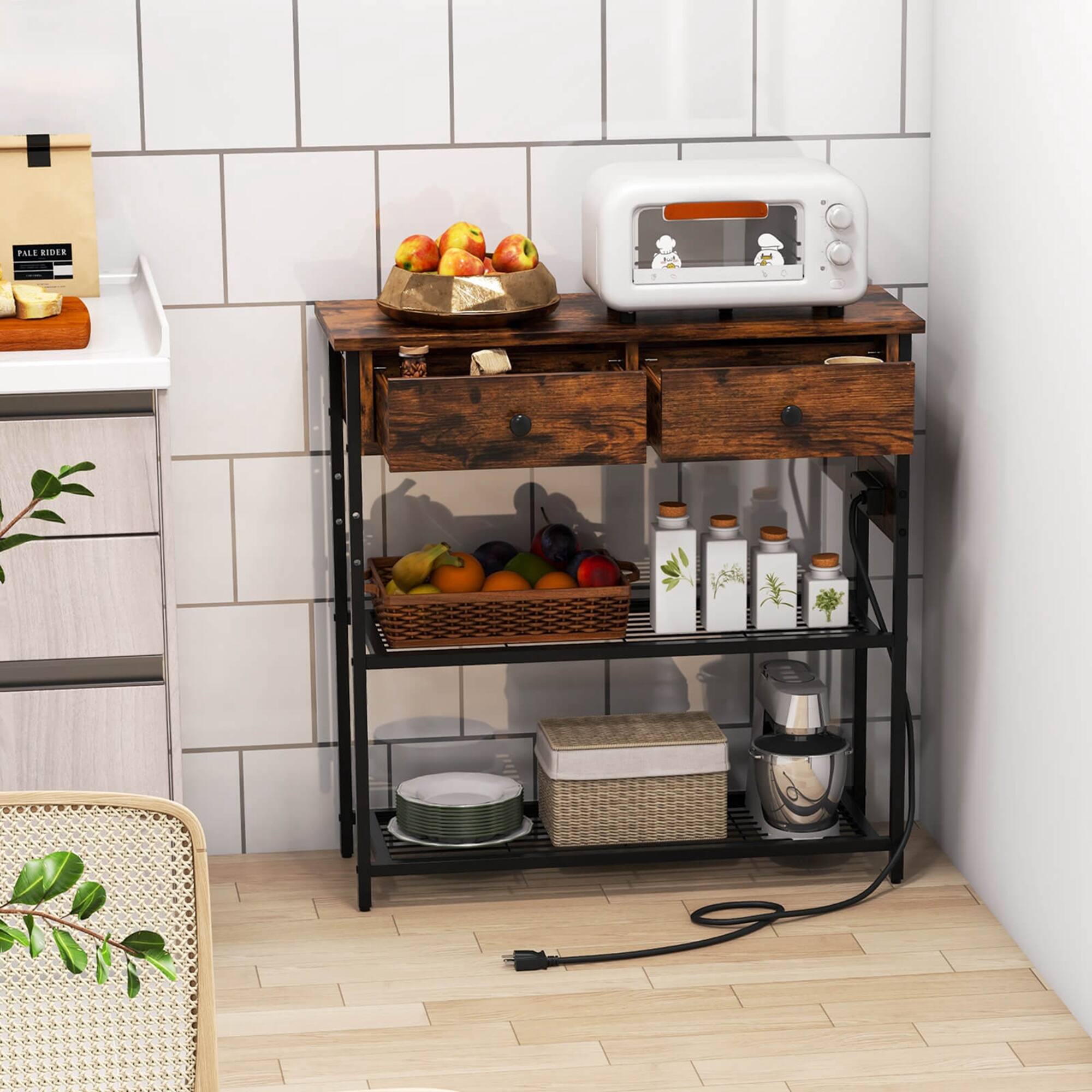 The image shows a kitchen with a microwave on top of a wooden stand, a sink nearby, and a bowl of fruit on the counter. There are also several bottles and a bowl of fruit on the counter. The kitchen is equipped with a microwave and a sink, and there is a chair in the room. The scene appears to be a cozy and functional space for cooking and dining.