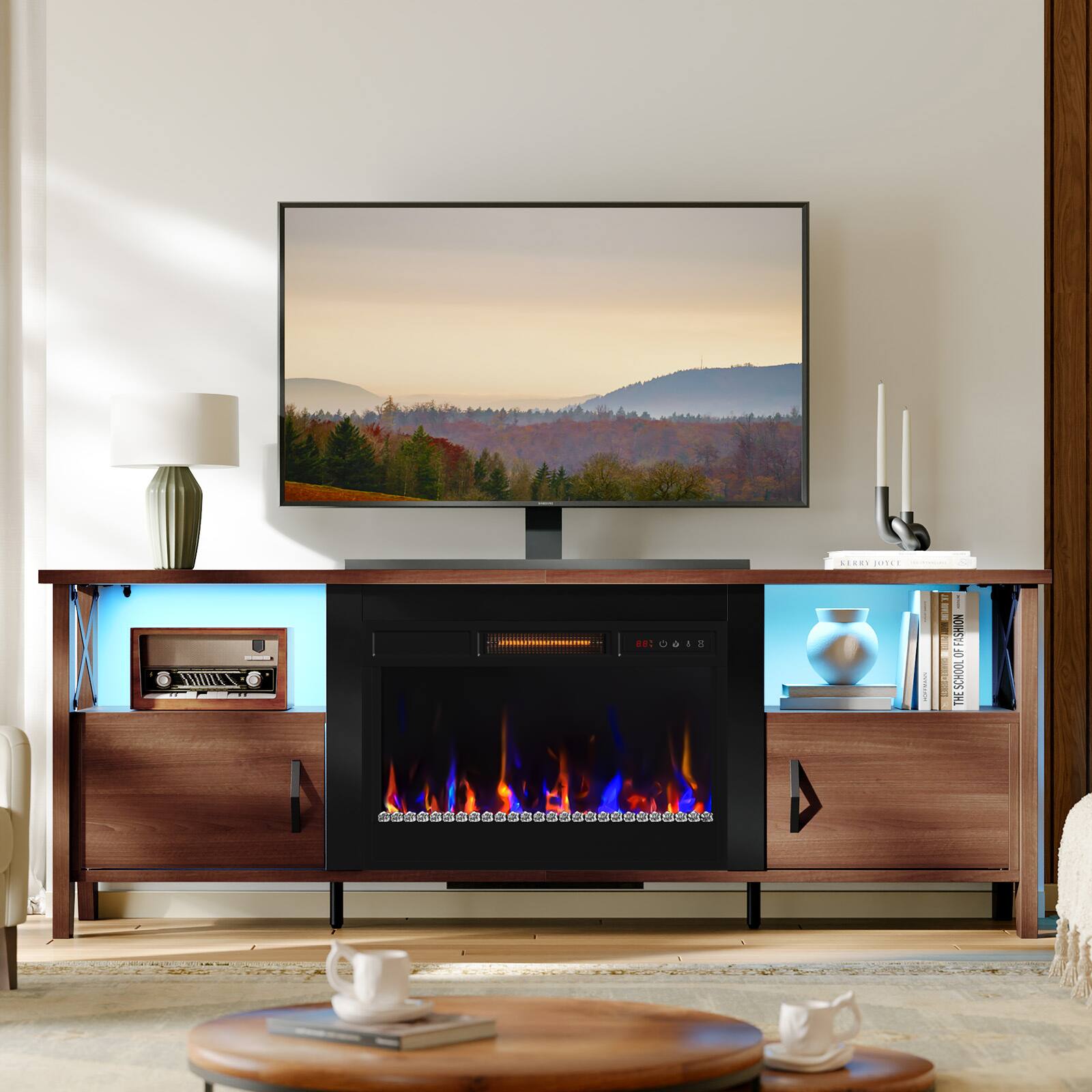 The image features a television sitting on top of a wooden entertainment center. The television is turned on and displaying a fireplace scene. The entertainment center also has a fireplace built into it, adding a cozy ambiance to the room. 

In addition to the television and fireplace, there are several books placed on the entertainment center, as well as a cup and a vase. A potted plant is also present in the room, adding a touch of greenery to the space. The overall setting appears to be a comfortable and inviting living area.