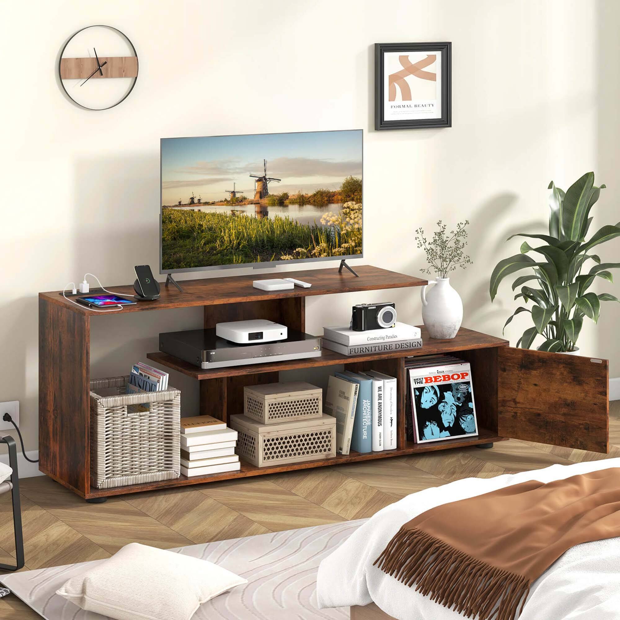 Furniture re-design aside, we have a TV on a wooden stand with a clock on the wall above it. The stand also has a laptop, a mouse, and a keyboard. There are books on the stand, and a potted plant is placed nearby. The room also features a bed with a comforter and a pillow.